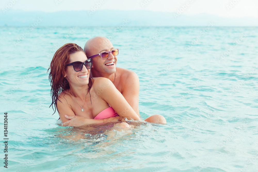 Cheerful couple embracing and posing in the water sea on a sunny
