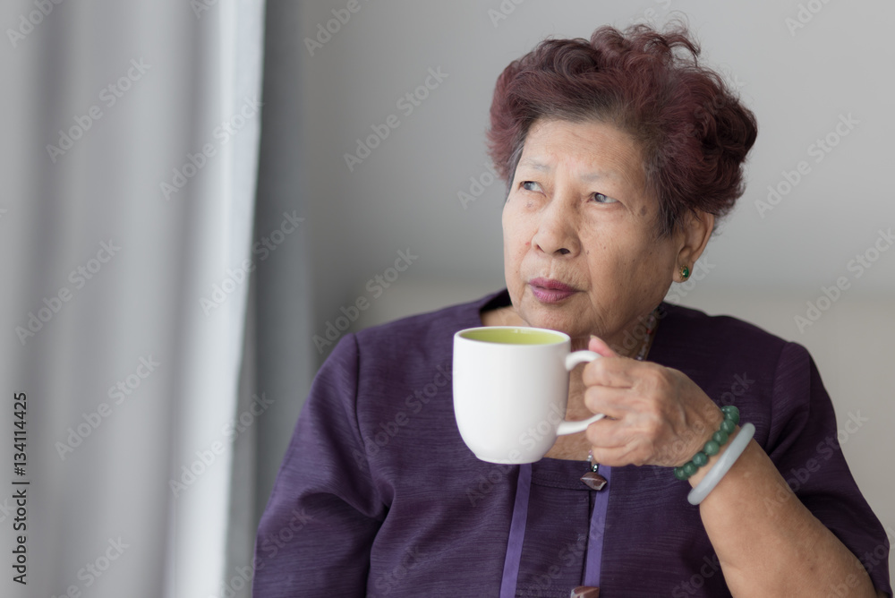 Asian senior woman drink a cup of tea near window with warm ligh Asian senior woman drink a cup of tea near window with warm ligh