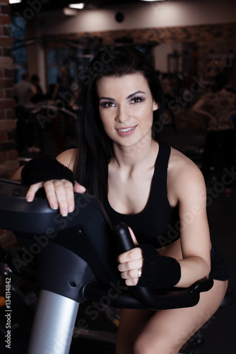 Muscular young woman wearing sportswear training on exercise bikes in gym. Intense cardio workout.
