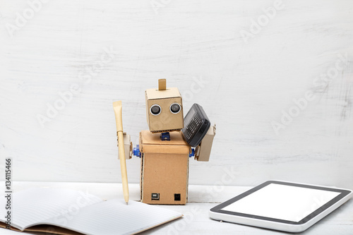 The robot holds a pen and the phone is near  laptop. Work