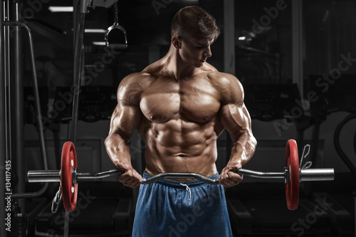 Muscular man working out in gym doing exercises with barbell, strong male naked torso abs