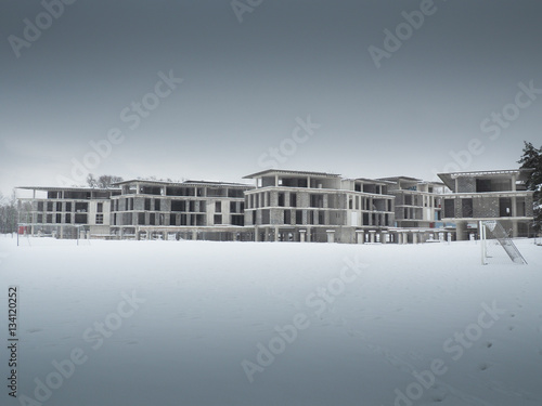 A large construction site stands in a winter setting, showing a group of connected structures with flat roofs and wide window openings. 