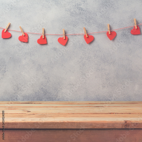 Empty wooden deck table over rustic wall background with heart shape garland. Valentines day concept