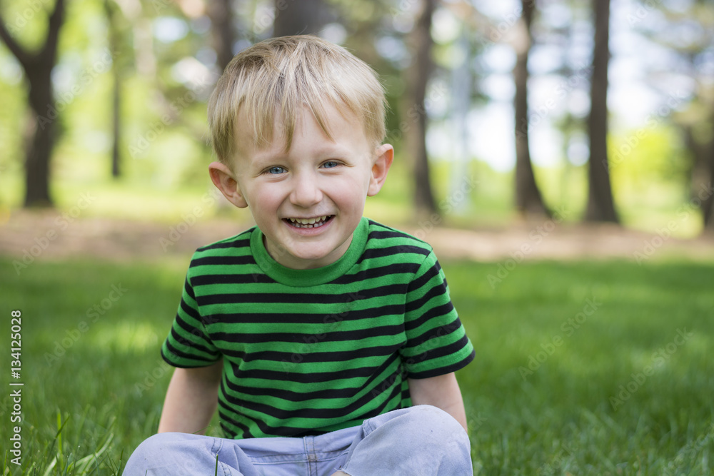 Happy young boy sitting in the grass at the park Happy young boy sitting in the grass at the park