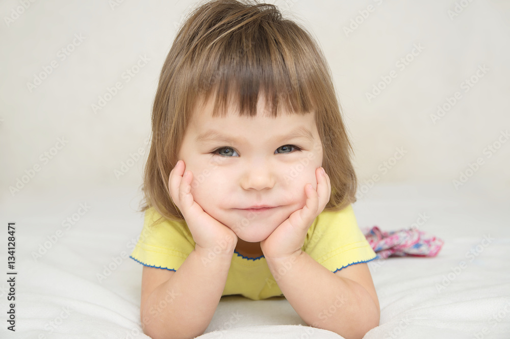 smiling happy little girl portrait with cute cheeks expressive positive emotional face lying on bed isolated, happy childhood concept smiling happy little girl portrait with cute cheeks expressive positive emotional face lying on bed isolated, happy childhood concept