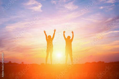 Silhouette of happy people making high hands in sunset sky backg