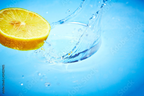 Fetta di limone cade nell'acqua con splash fondo blu
