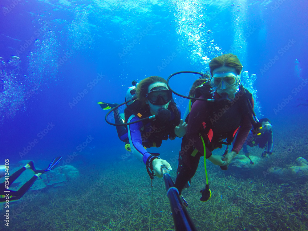 Underwater couple scuba diving selfie shot with selfie stick. Deep blue sea. Wide angle shot. Underwater couple scuba diving selfie shot with selfie stick. Deep blue sea. Wide angle shot.