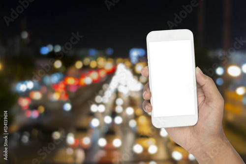 Closeup of hand holding modern smart phone with blank screen for your text with night light bokeh
