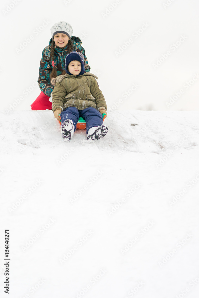Mother baby winter rolls from the mountain on a sled in the snow Mother baby winter rolls from the mountain on a sled in the snow