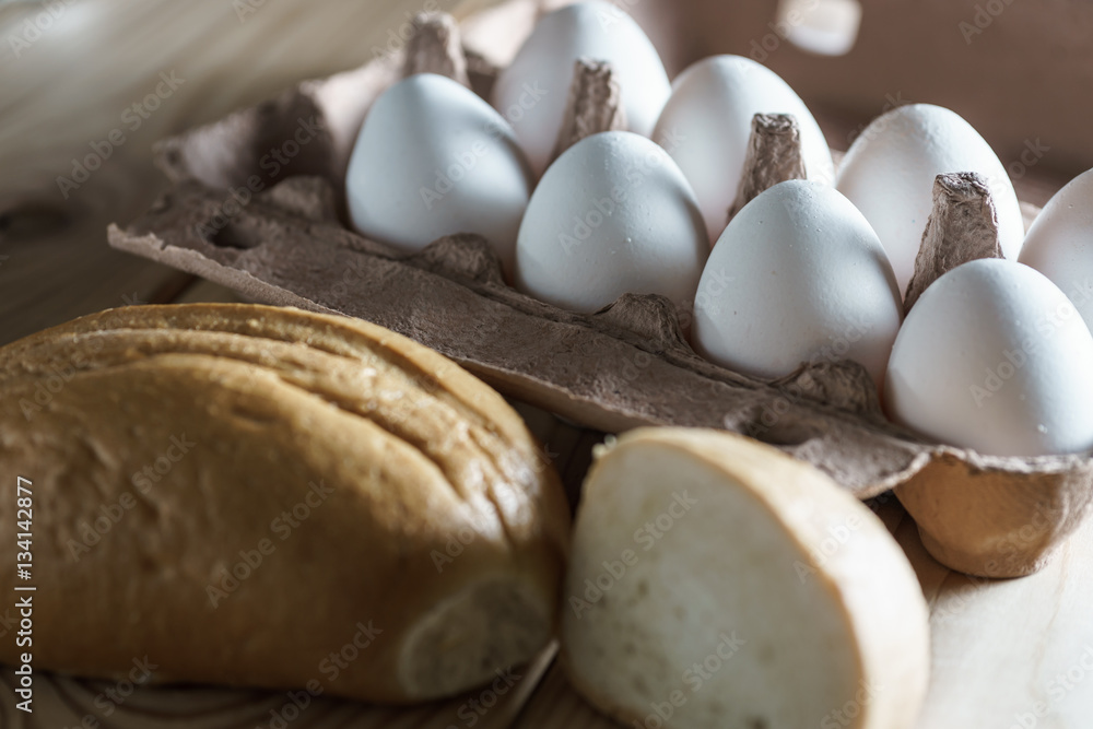 opened cardboard egg box with white eggs and bread on a wooden background. opened cardboard egg box with white eggs and bread on a wooden background.