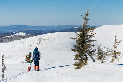 A guy and a girl trekking with backpacks in winter sunny mountai