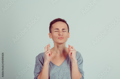 Closeup portrait of a girl short hair style boy alike woman with fingers crossed gesture eyes closed wishing for better future isolated on a green white background. Horizontal studio shot
