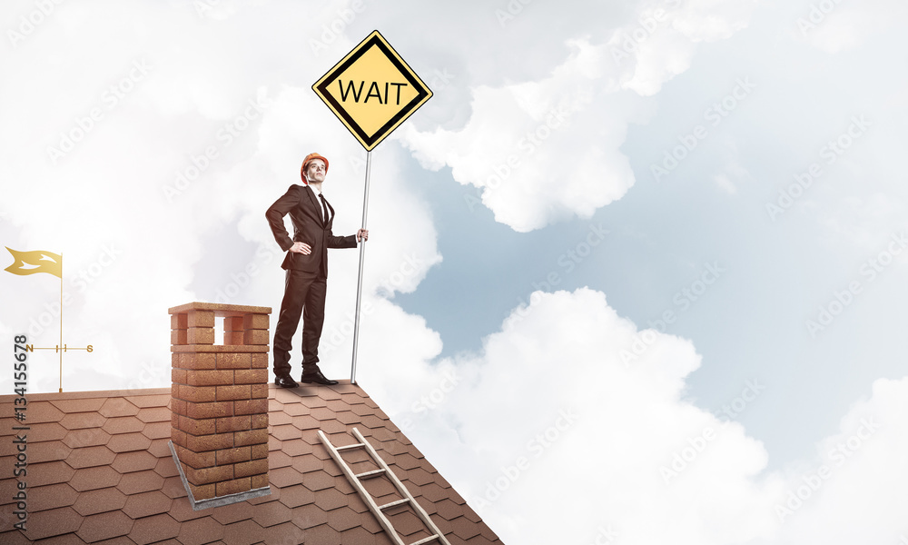 Young businessman on house brick roof holding yellow signboard. Young businessman on house brick roof holding yellow signboard.