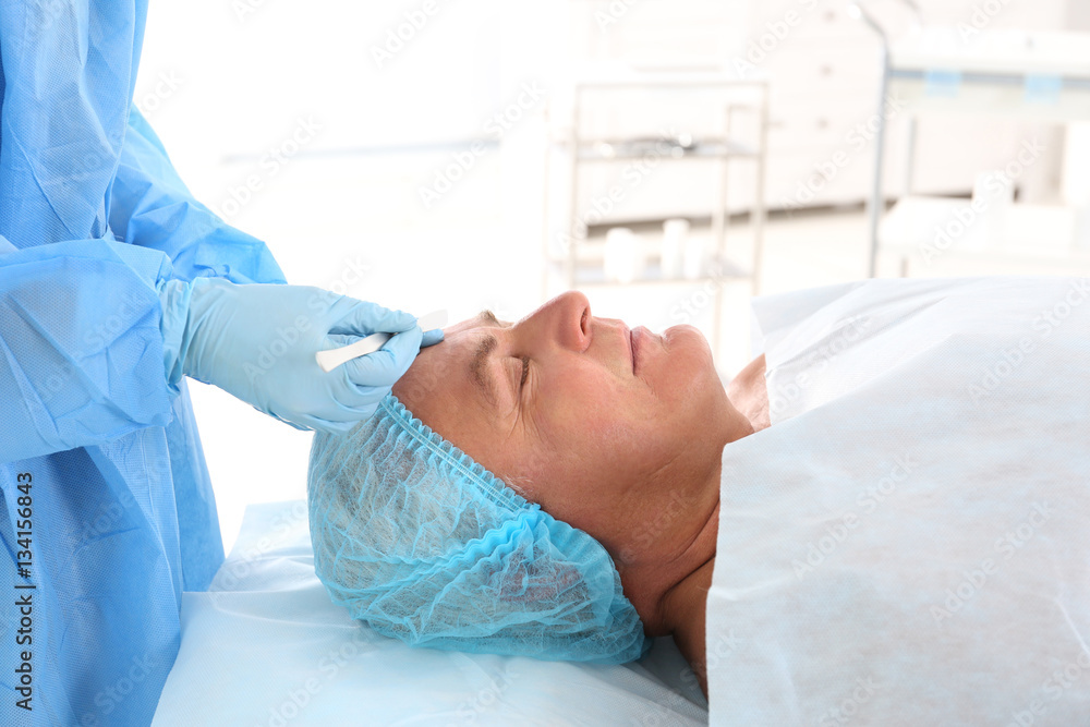 Fototapeta premium Surgeon hands with scalpel near senior man face