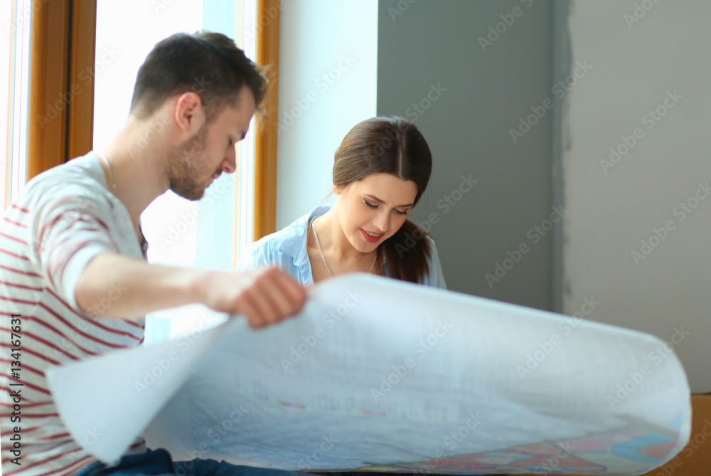 Obraz premium Young couple sitting on the floor and looking at the blueprint of new home
