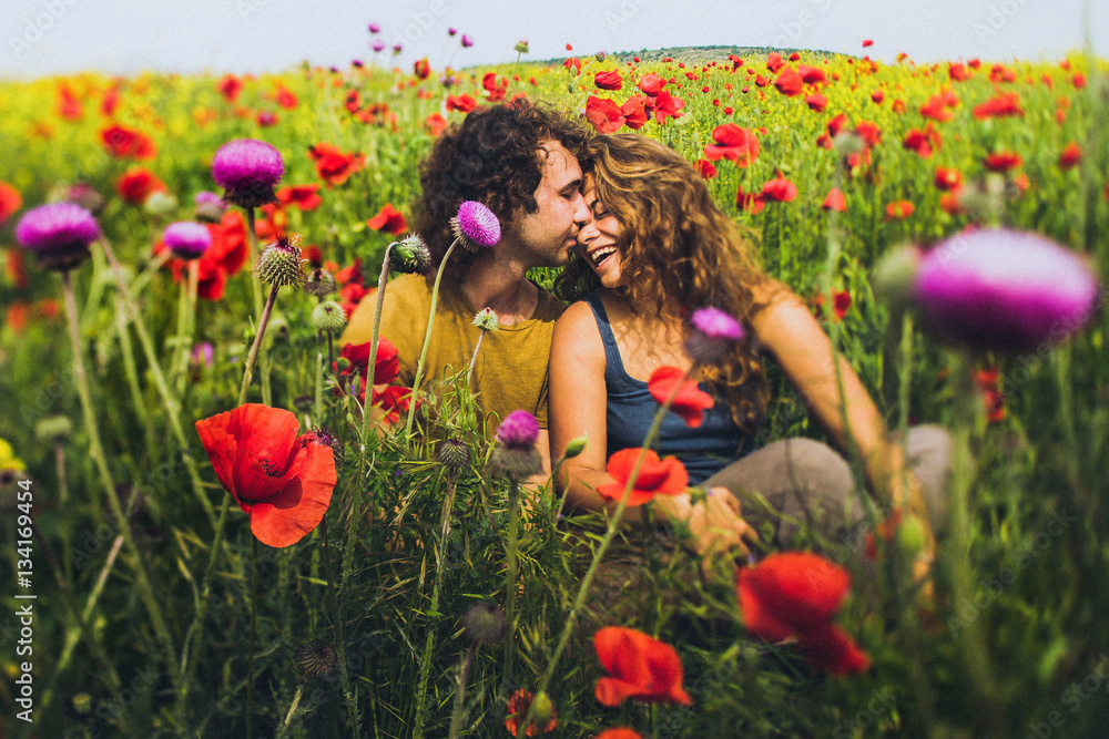Young happy couple with curly hair enjoying in bright red and yellow blossoming field Young happy couple with curly hair enjoying in bright red and yellow blossoming field