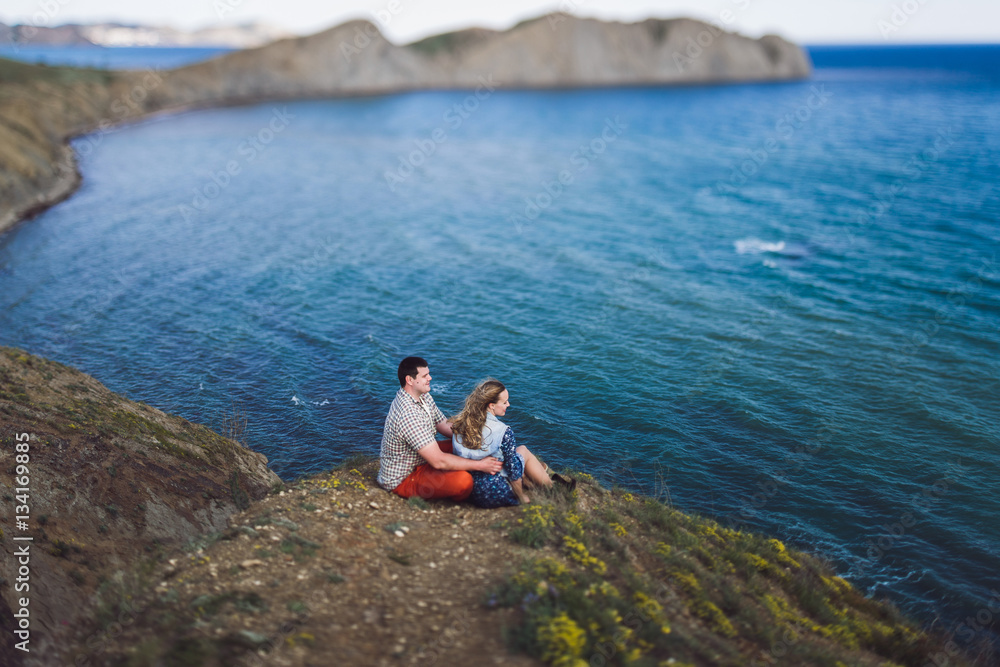 Couple relaxing by the sea with amazing mountain view. Jeans jacket and blue skirt