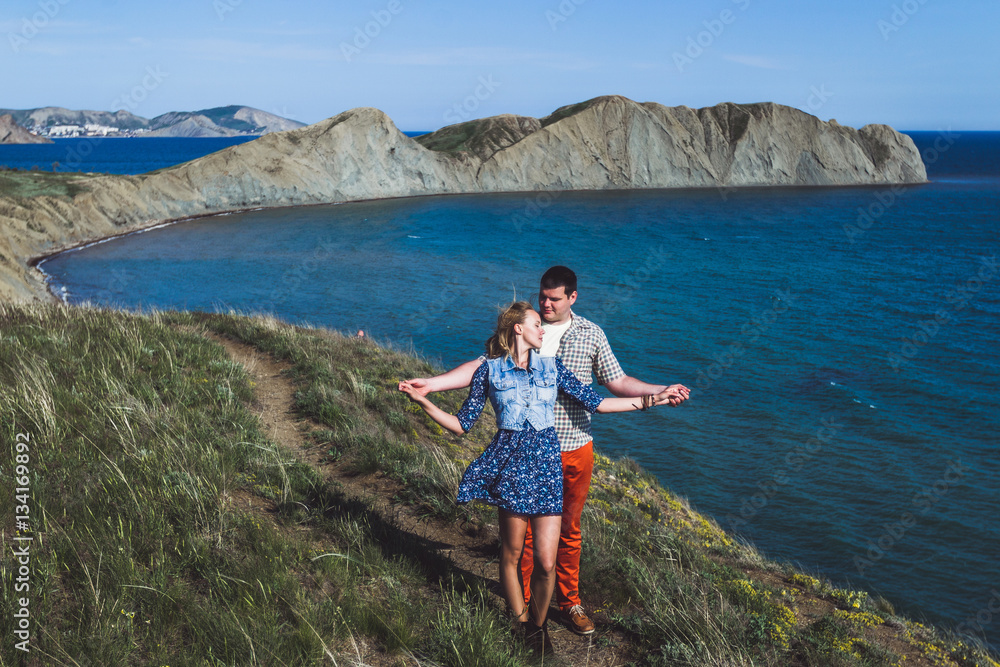 Couple relaxing by the sea with amazing mountain view. Jeans jacket and blue skirt