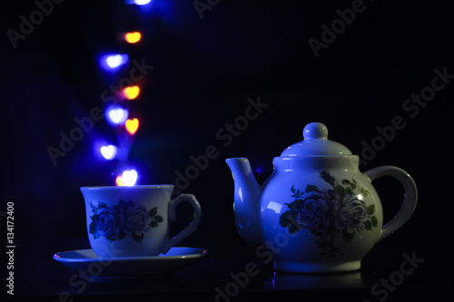 A mysterious ceramic tea pot and a steaming tea cup bubbling heart-shaped, colorful bubbles up in the air