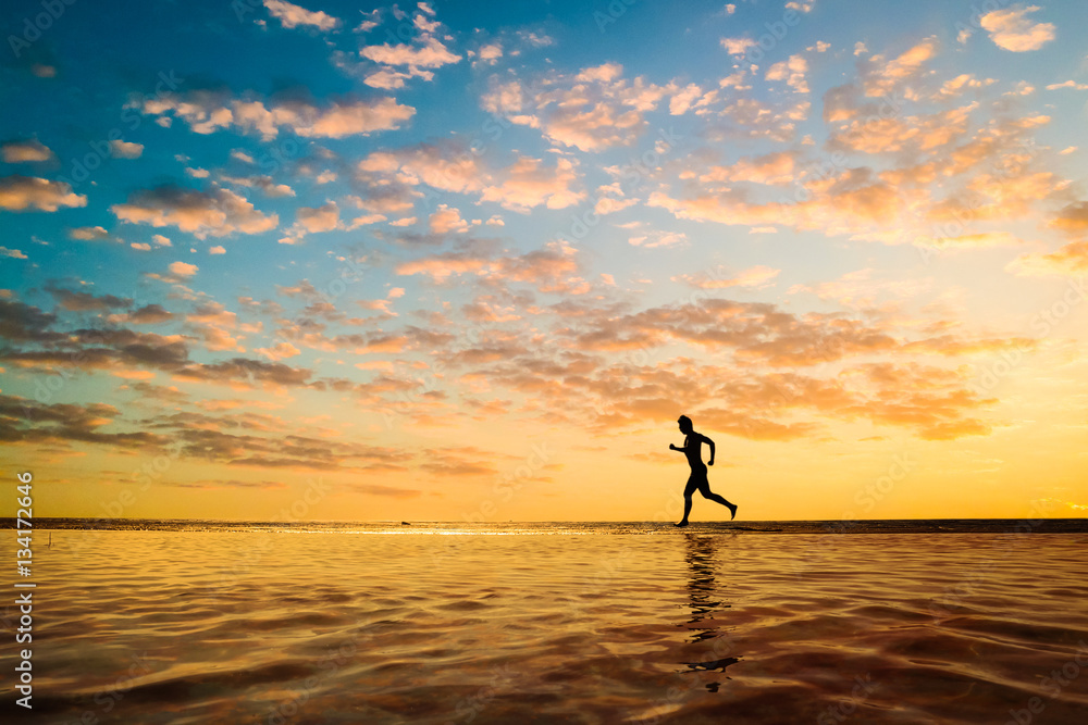 Silhouette of a young man running along the beach of the sea during an amazing sunset.