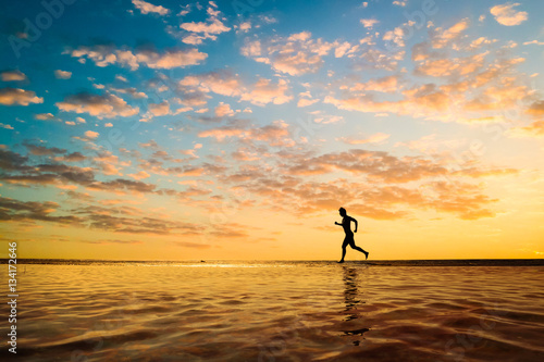 Silhouette of a young man running along the beach of the sea during an amazing sunset.