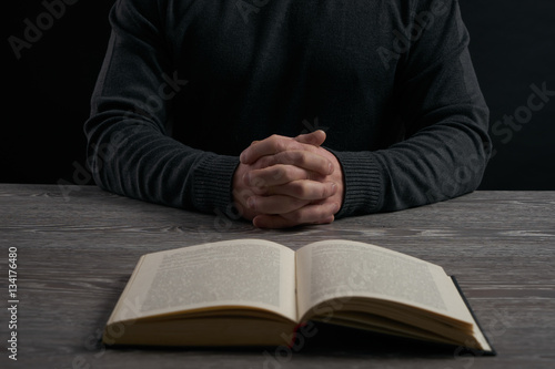 Open book and praying hands of a man on wooden table. Religion concept