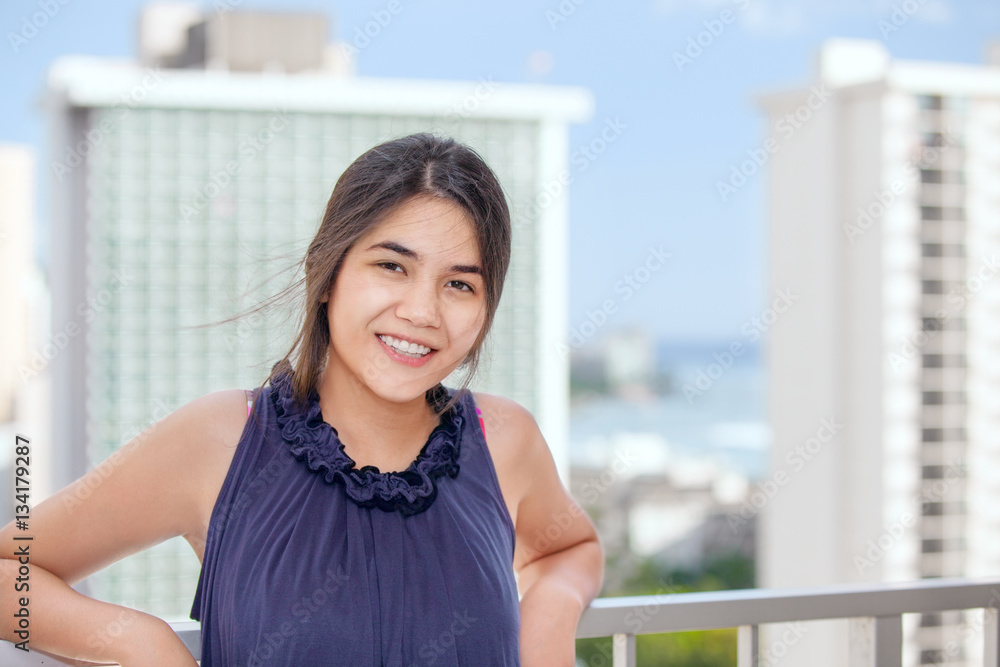Smiling biracial teen girl on outdoor highrise patio, ocean  bac