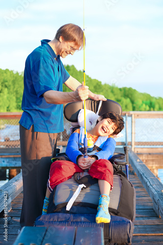 Caucasian father helping disabled ten year old son in wheelchair fish off pier