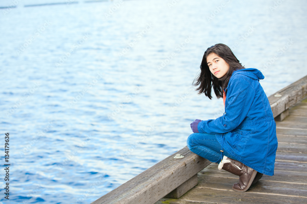 Sad, lonely biracial  teen girl on wooden pier by water