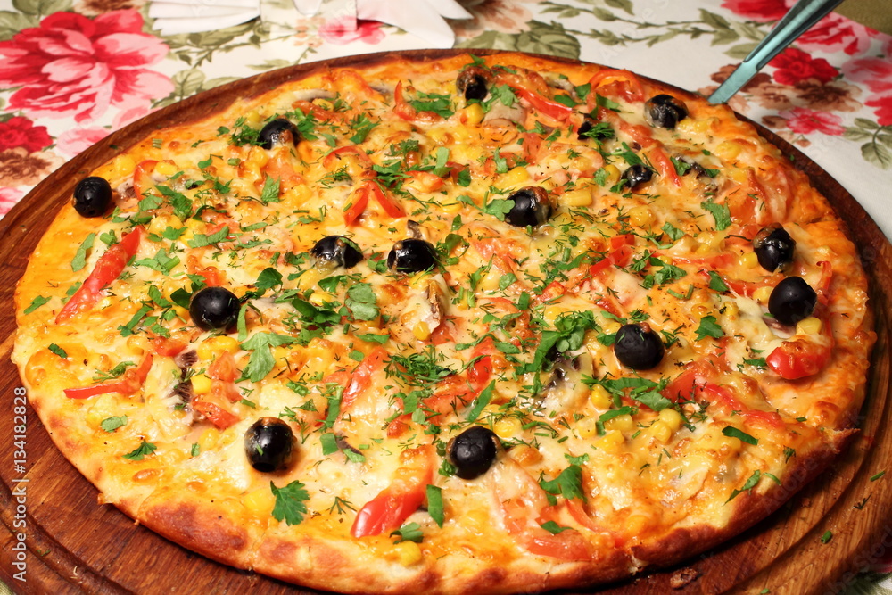 Pizza with chicken, olives, corn, red bell pepper and parsley on a wooden round board