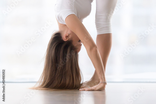 Young woman practicing yoga, standing in head to knees, uttanasana exercise, Standing forward bend pose, working out, wearing sportswear, white t-shirt, pants, close up