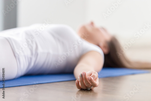 Closeup of young attractive woman practicing yoga, lying in Savasana exercise, Dead Body, Corpse pose, working out, wearing sportswear, white t-shirt, indoor, fingers in focus
