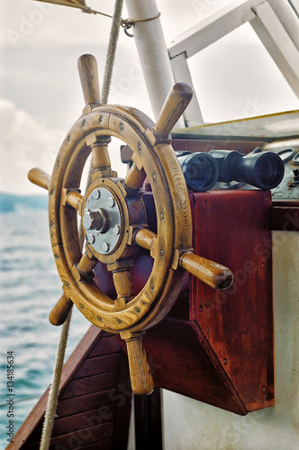 Yacht's steering wheel and binoculars vertical close up view on sea background