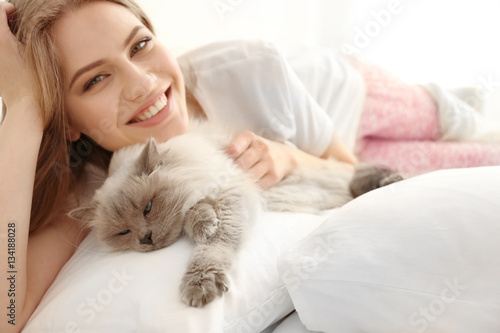 Beautiful young woman with cute cat lying on bed at home