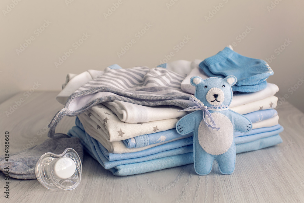 baby clothes with diapers are stacked with a pacifier and a toy bear