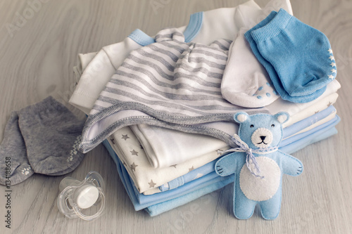 baby clothes with diapers are stacked with a pacifier and a toy bear photo