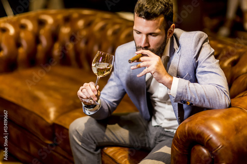 Young man tasting white wine and smoking cigar photo