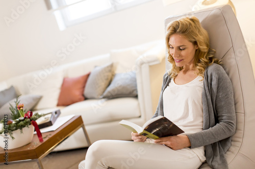 Young woman reading a book and sitting on comfortable chair at h