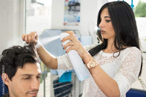 Young female hairdresser applying spray on client's hair at hair in salon.