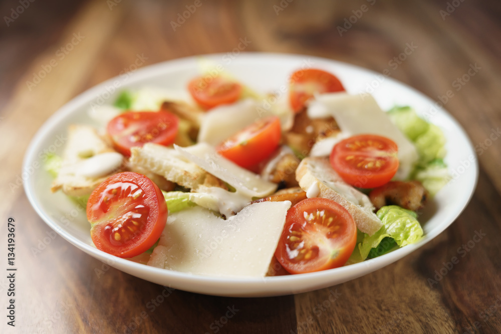 fresh homemade caesar salad with chicken and cherry tomatoes on wood table, shallow depth of field