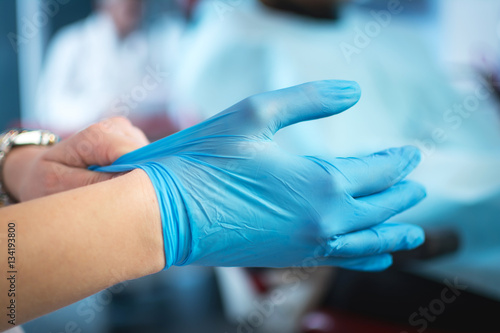 Close up of female doctor s hands putting on blue sterilized surgical gloves in the office.