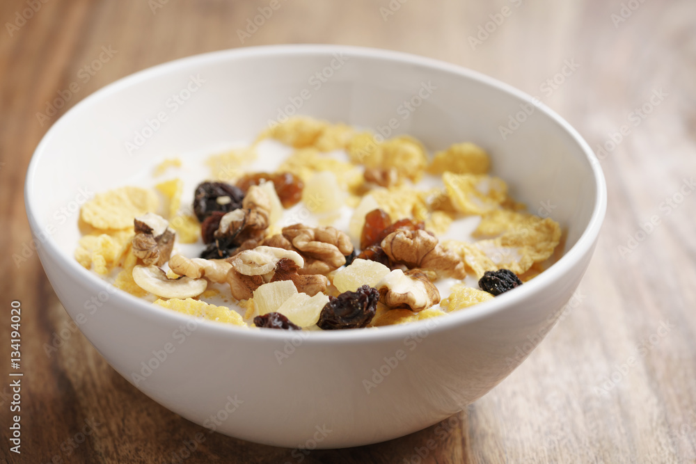 closeup photo of corn flakes with fruits and nuts in white bowl on wood table, simple healthy breakfast closeup photo of corn flakes with fruits and nuts in white bowl on wood table, simple healthy breakfast