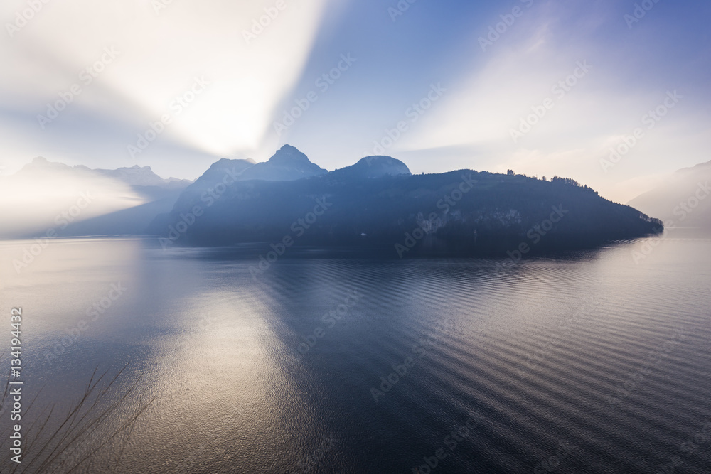 Fototapeta premium Alps of central Switzerland. Grand game of light and shadow. Sunlight sat behind a mountain ridge. Rays of light pierce the. Extra wide lens
