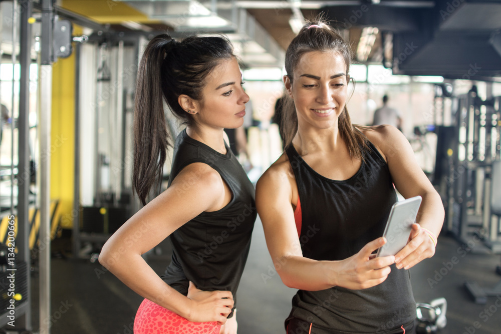 Obraz premium Two female friends taking a selfie photo after hard workout in gym.