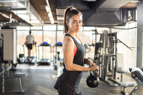 Attractive sporty girl doing exercises with kettlebell in a gym.