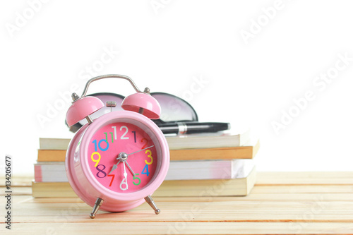 Pink alarm clock placed on a wooden table on a white back ground