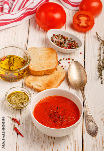 Delicious tomato soup with spices and fresh herbs. Olive oil, pepper, tomatoes, thyme and toasted bread on the table. Selective focus
