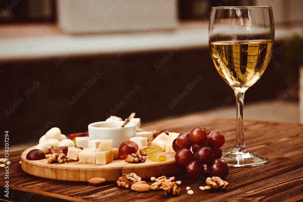Cheese Board served with grapes, nuts and a glass of white wine on a wooden background