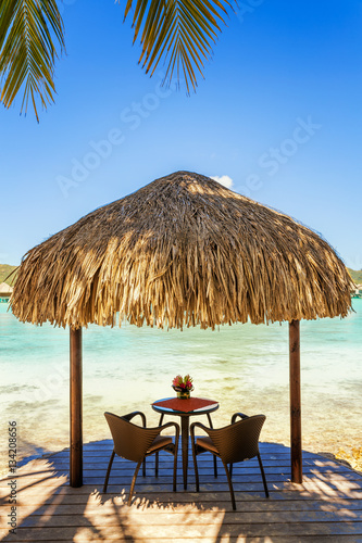 Fototapeta Naklejka Na Ścianę i Meble -  Two chairs and coffee table under a thatched parasol on a sand b